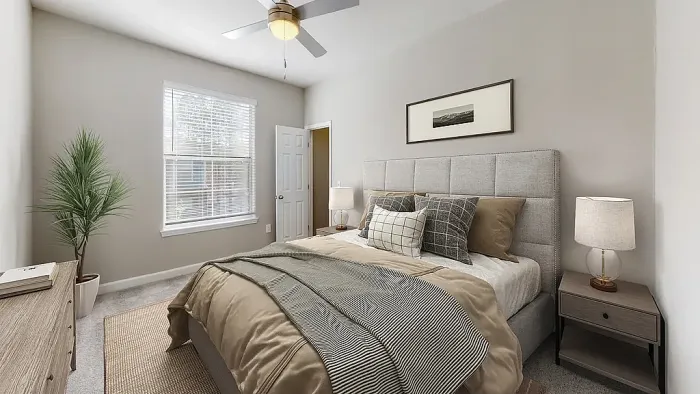 Bright, modern bedroom featuring a neutral color palette, upholstered bed with layered bedding, soft carpeting, bedside lighting, ceiling fan, and large window with natural light.