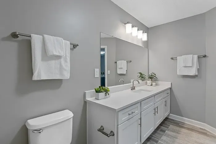 Spacious bathroom featuring a dual-sink white vanity, oversized mirror, modern lighting, wood-style flooring, and a clean neutral design with contemporary finishes.