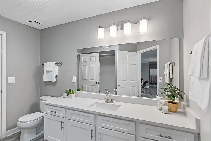 Bright contemporary bathroom with an oversized framed mirror, expansive white vanity, modern lighting, sleek fixtures, and a clean neutral color palette.