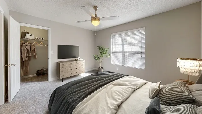Spacious bedroom with plush carpeting, ceiling fan, large window with natural light, walk-in closet access, and modern neutral furnishings for a warm, relaxing atmosphere.