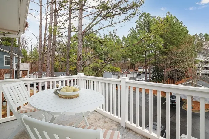 Private outdoor balcony with seating area, peaceful wooded views, and a bright open-air setting perfect for relaxing or enjoying morning coffee.