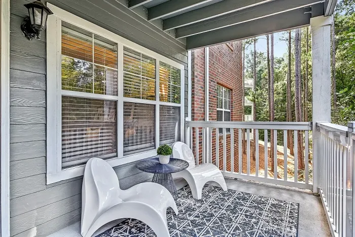 Covered private balcony with cozy seating area, wooded community views, and a relaxing outdoor space ideal for enjoying fresh air and quiet surroundings.