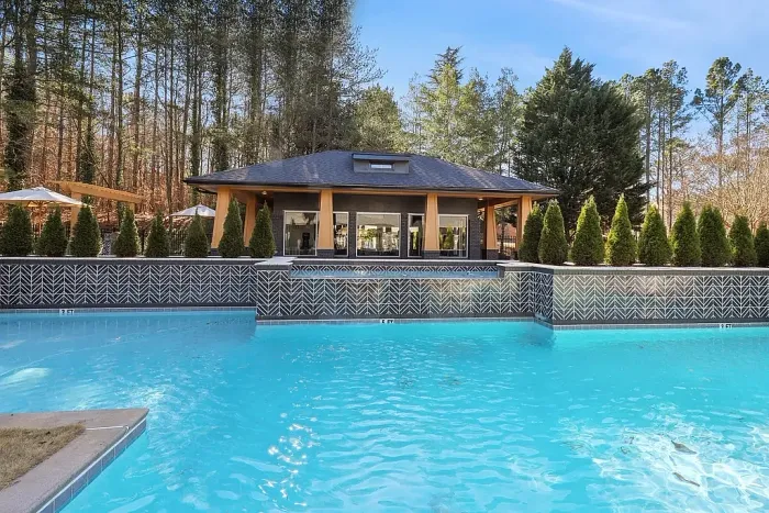 Resort-style swimming pool with striking tile accents, crystal-clear water, and a modern clubhouse surrounded by scenic wooded views and landscaped greenery.