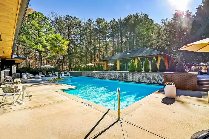 Resort-style swimming pool with expansive sundeck seating, modern clubhouse views, and peaceful wooded surroundings creating a relaxing outdoor retreat.