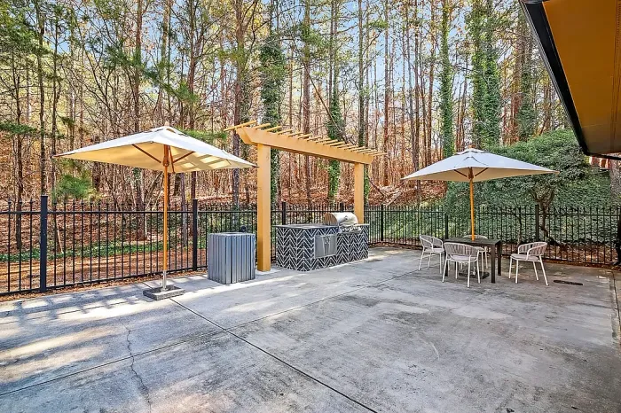 Outdoor entertainment area featuring a pergola-covered grilling station, shaded dining spaces, and serene wooded surroundings perfect for relaxing or gathering with friends.