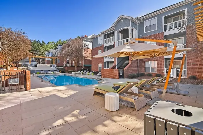 Resort-style swimming pool with luxurious lounge seating, shaded sunbeds, and beautifully maintained outdoor spaces surrounded by modern apartment homes.