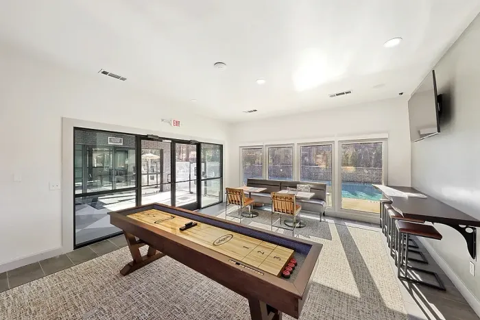 Stylish resident clubhouse featuring shuffleboard, lounge seating, entertainment space, and relaxing poolside views through expansive windows.