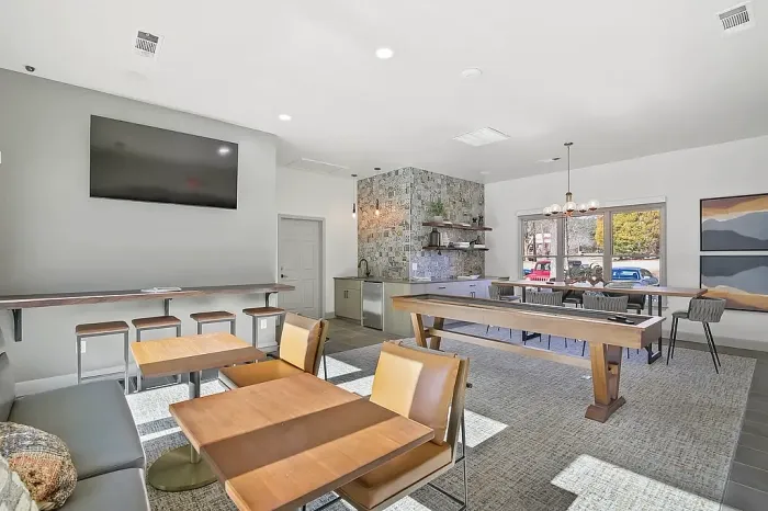 Stylish resident clubhouse featuring shuffleboard, lounge seating, entertainment space, and relaxing poolside views through expansive windows.