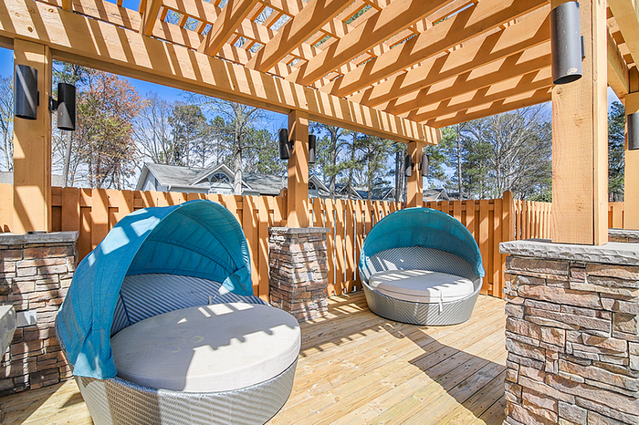 Charming outdoor patio with stylish stone accents and round canopy loungers, ideal for relaxation under a sunlit pergola.