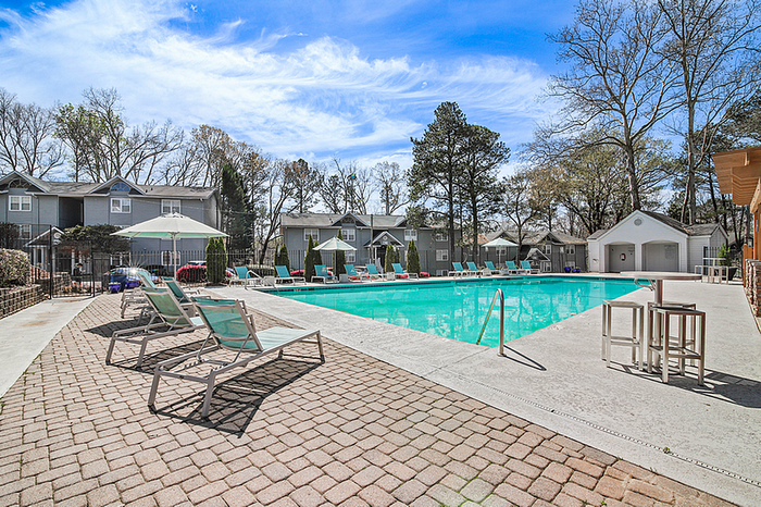 Inviting apartment community with a sparkling pool, comfortable loungers, and vibrant umbrellas under a clear blue sky.