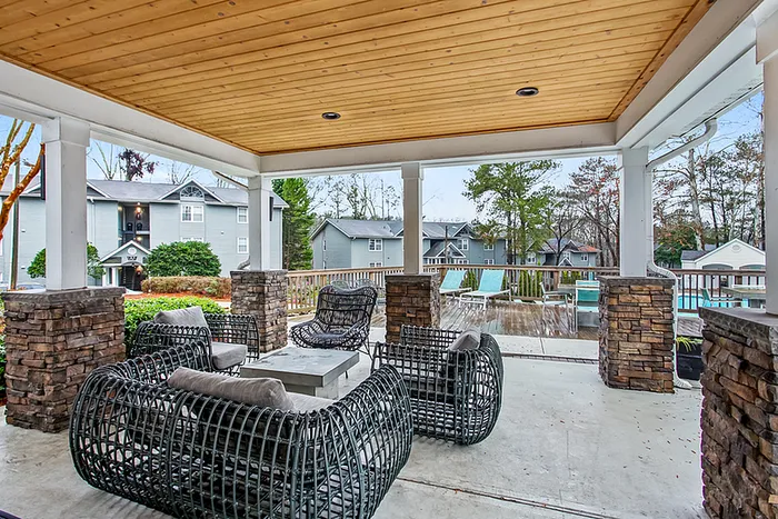 Charming outdoor patio with stylish wicker furniture and scenic views of lush greenery and a sparkling pool.