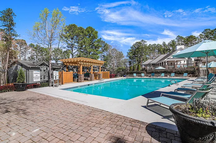 Inviting outdoor pool area with modern lounge chairs, surrounded by vibrant greenery and a charming wooden pergola, perfect for relaxing under the sun.