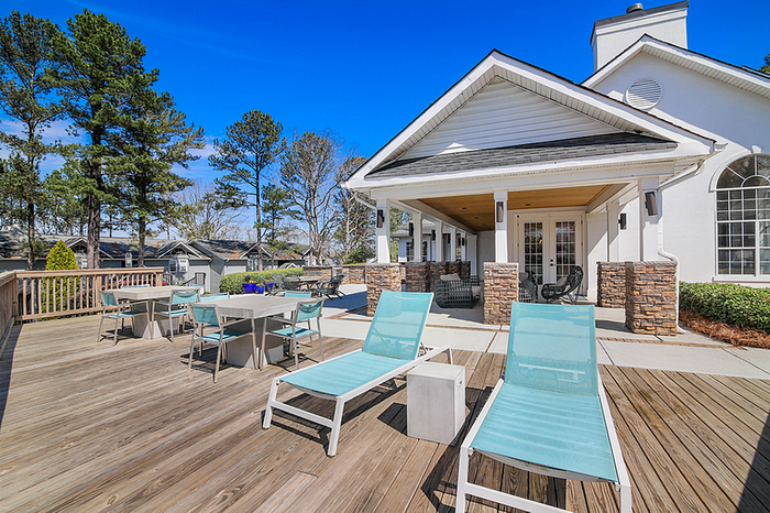 Inviting outdoor patio with chic lounge chairs, dining tables, and a cozy clubhouse surrounded by lush trees and clear blue skies.