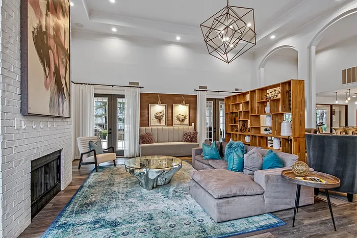 Elegant clubhouse with modern chandelier, cozy fireplace, stylish artwork, and plush sectional sofa accented by vibrant teal cushions.