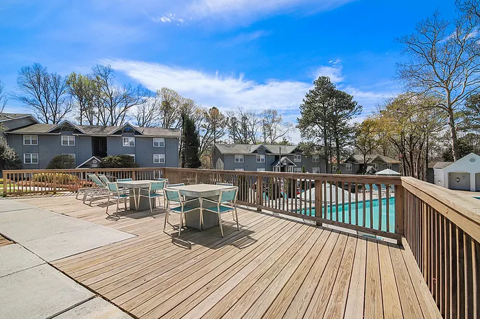 Charming apartment community with spacious wooden deck overlooking a pristine pool, surrounded by lush greenery and stylish buildings.