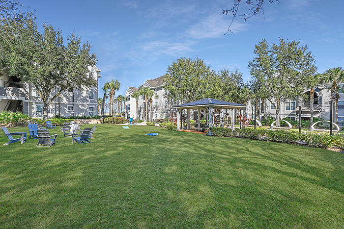 Charming community outdoor space with lush green lawns, cozy seating, and a modern gazebo under a clear blue sky.
