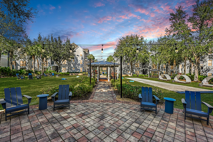 Charming outdoor patio scene with vibrant Adirondack chairs, lush greenery, and a serene garden path under a colorful sunset sky.