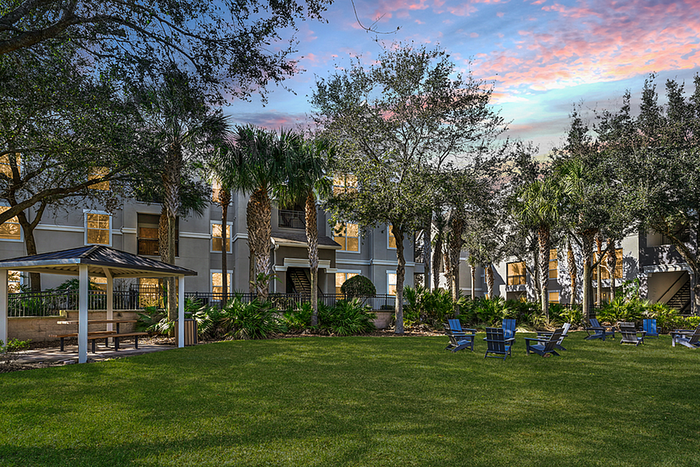 Charming apartment community with lush greenery, outdoor seating, and a gazebo at sunset, offering a serene and picturesque living environment.