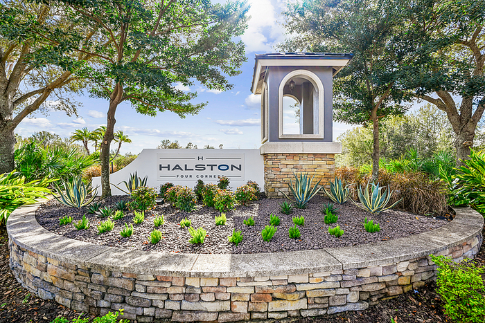 Inviting landscaped entrance to Halston Four Corners, featuring lush greenery and elegant stone detailing.