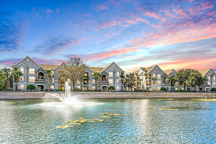 Charming apartment community with elegant architecture and a serene water fountain under a stunning sunset sky.