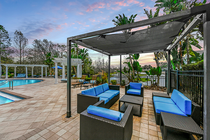 Luxurious outdoor lounge with chic blue seating, adjacent to a swimming pool, surrounded by lush greenery and a serene landscape.