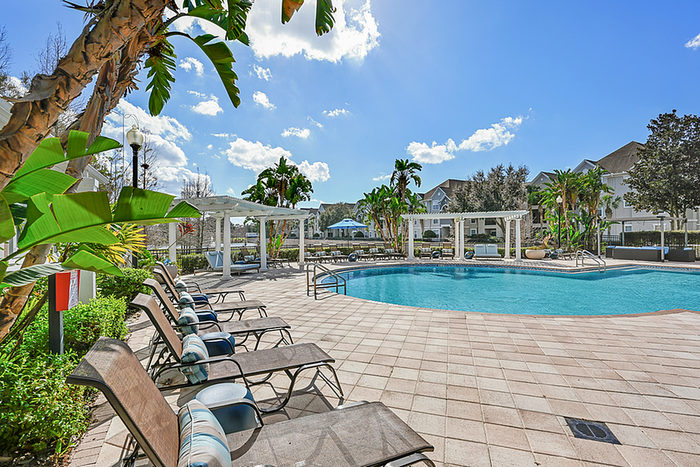 Resort-style pool area with elegant lounge chairs and lush tropical landscaping under a clear blue sky.