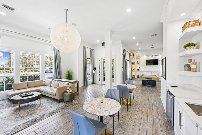 Inviting open-concept clubhouse with modern decor, featuring a comfortable seating area, large windows for natural light, and a stylish dining setup.