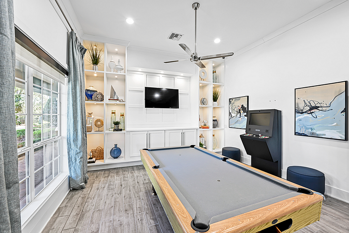 Bright and stylish game room with a pool table, large windows, built-in shelving, and modern décor.