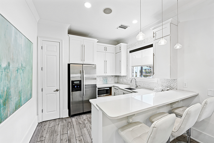 Modern clubhouse kitchen with sleek white cabinetry, stainless steel refrigerator, and a stylish breakfast bar with pendant lighting.