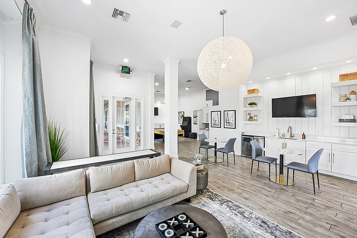 Bright and modern clubhouse featuring elegant decor, a comfortable sectional sofa, and a sleek, open kitchen with contemporary furnishings.