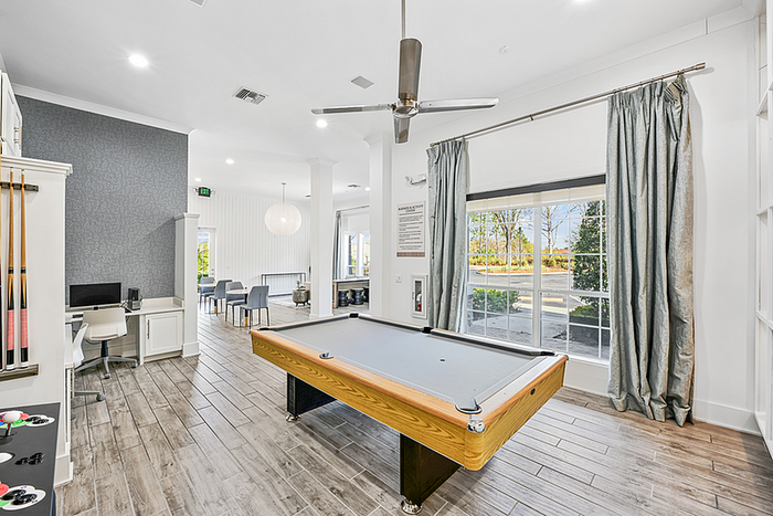Elegant game room featuring a modern pool table and cozy seating area with large windows overlooking lush greenery.