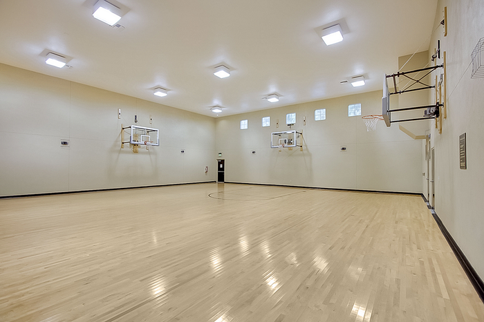 Spacious indoor basketball court with polished hardwood flooring, ceiling lights, and multiple basketball hoops for an active lifestyle.