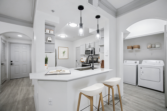 Modern kitchen with sleek countertops and pendant lighting, featuring built-in laundry appliances and stylish seating.