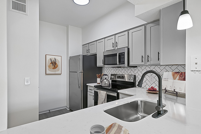 Modern kitchen with sleek gray cabinets, stainless steel appliances, and elegant herringbone backsplash, featuring a polished countertop with a stylish sink and contemporary lighting.