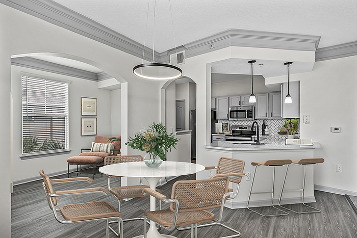 Modern apartment interior featuring an open dining area with a round table, stylish chairs, and a cozy seating nook. The adjacent kitchen boasts sleek cabinetry and pendant lighting, highlighting a contemporary elegance.