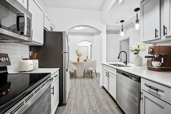 Modern kitchen with sleek stainless steel appliances, stylish white cabinetry, and inviting open archway leading to a dining area.