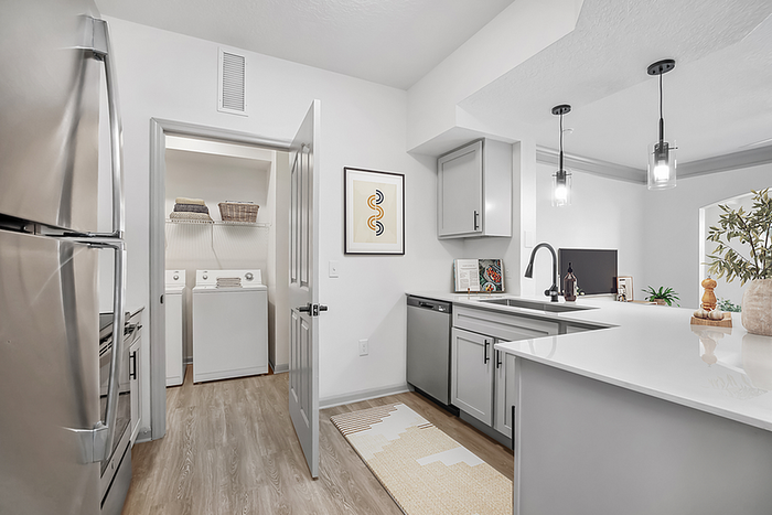 Modern kitchen with sleek stainless steel appliances, elegant pendant lighting, and an open view to a chic living area, complete with an adjacent laundry nook.