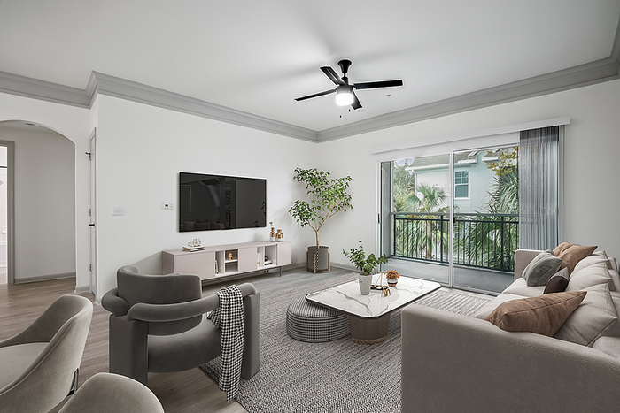 Elegant living room with modern furniture, sleek TV setup, and large sliding doors opening to a lush balcony view.