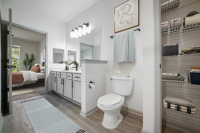 Modern bathroom with sleek cabinetry, elegant vanity, open closet shelving, and a glimpse of a cozy bedroom.