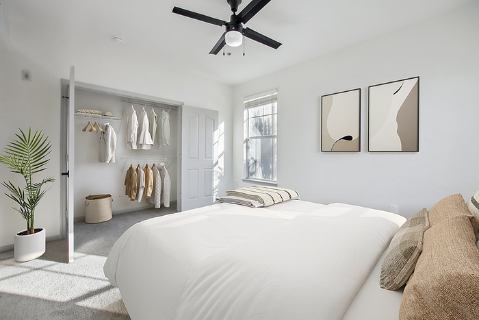 Bright and airy bedroom featuring minimalist decor, a spacious closet, modern ceiling fan, and tasteful wall art.