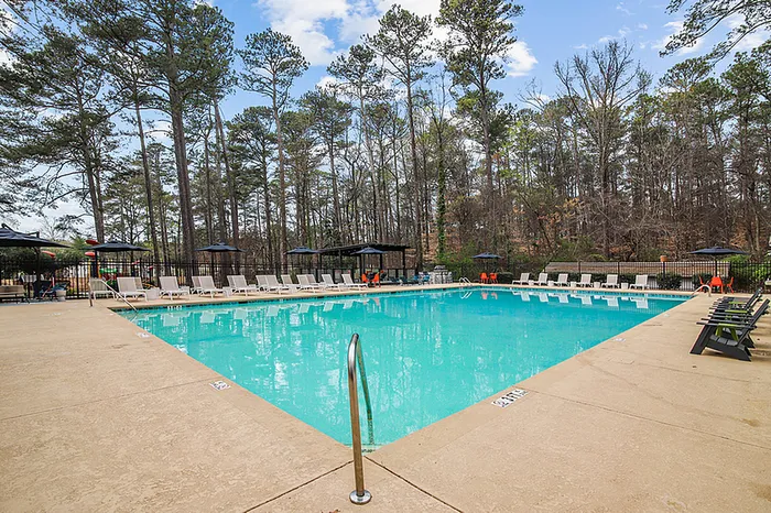 Inviting outdoor swimming pool surrounded by luxurious lounge chairs and set against a backdrop of lush trees, perfect for relaxation.