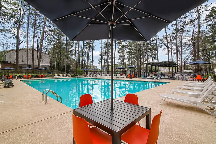 Inviting pool area with vibrant orange seating, surrounded by lush trees, perfect for relaxation and leisure.