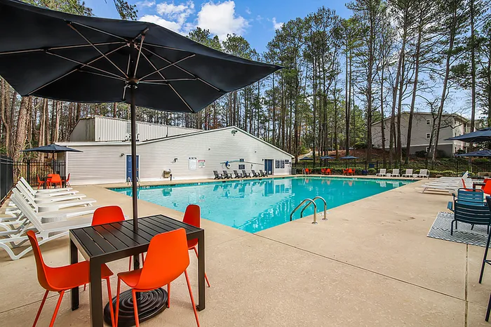 Inviting outdoor pool area with vibrant orange chairs and relaxing lounger seating, surrounded by lush trees and a serene atmosphere.