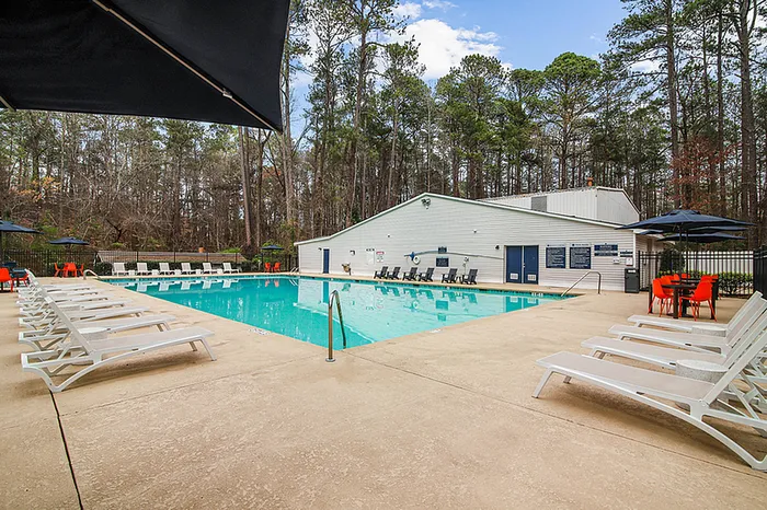 Inviting pool area surrounded by white lounge chairs and vibrant orange tables, nestled in a serene wooded setting.