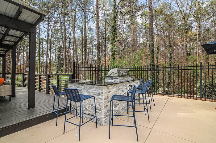 Chic outdoor patio with modern bar seating and grill, surrounded by lush forest views.