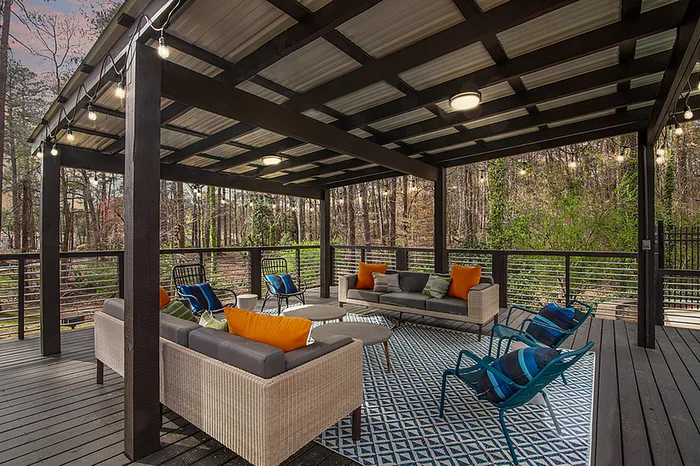Chic outdoor patio with stylish wicker furniture, vibrant cushions, and ambient string lights overlooking a lush, tranquil forest setting.