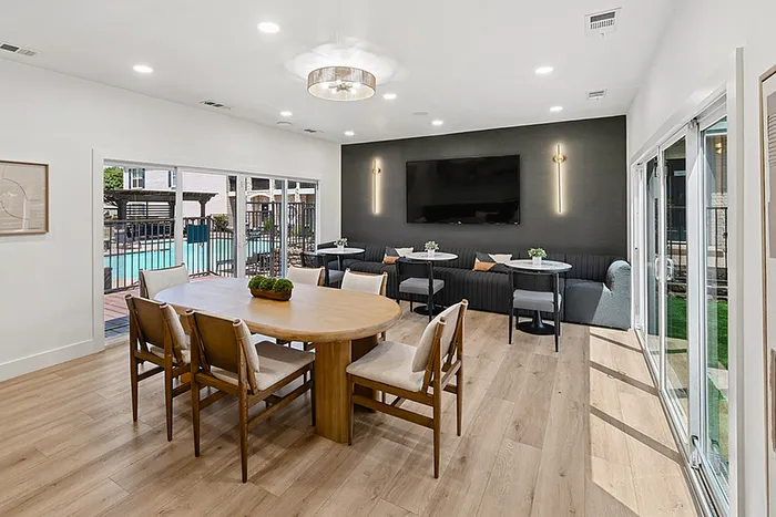 Elegant open-plan clubhouse with luxurious dining setup, modern decor, and large windows overlooking a serene pool area.