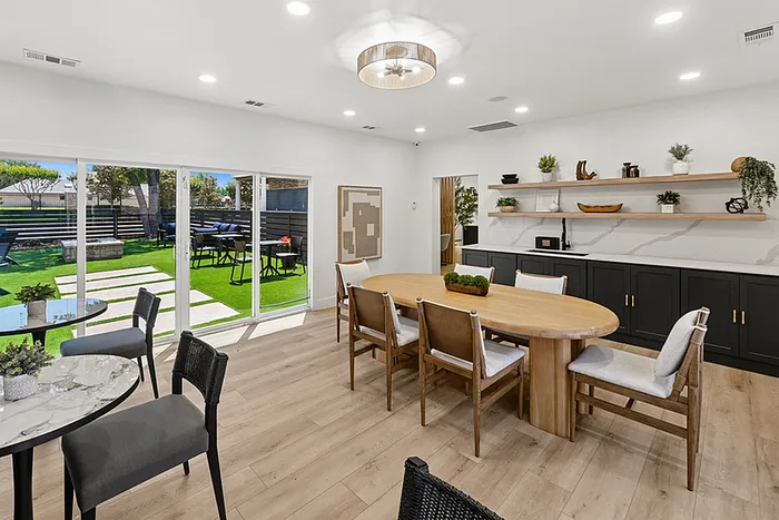 Bright, modern clubhouse with sleek wooden furniture opens to a lush green courtyard through sliding glass doors.