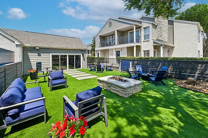 Charming apartment exterior with lush green lawn, cozy outdoor seating, vibrant flowers, and a modern fire pit, promising relaxation and outdoor enjoyment.
