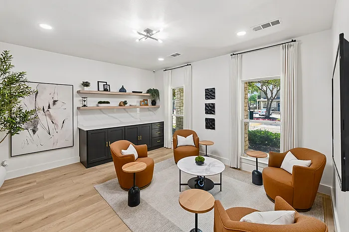 Elegant clubhouse featuring stylish orange armchairs, modern decor, and natural light pouring through large windows, creating a welcoming and sophisticated ambiance.